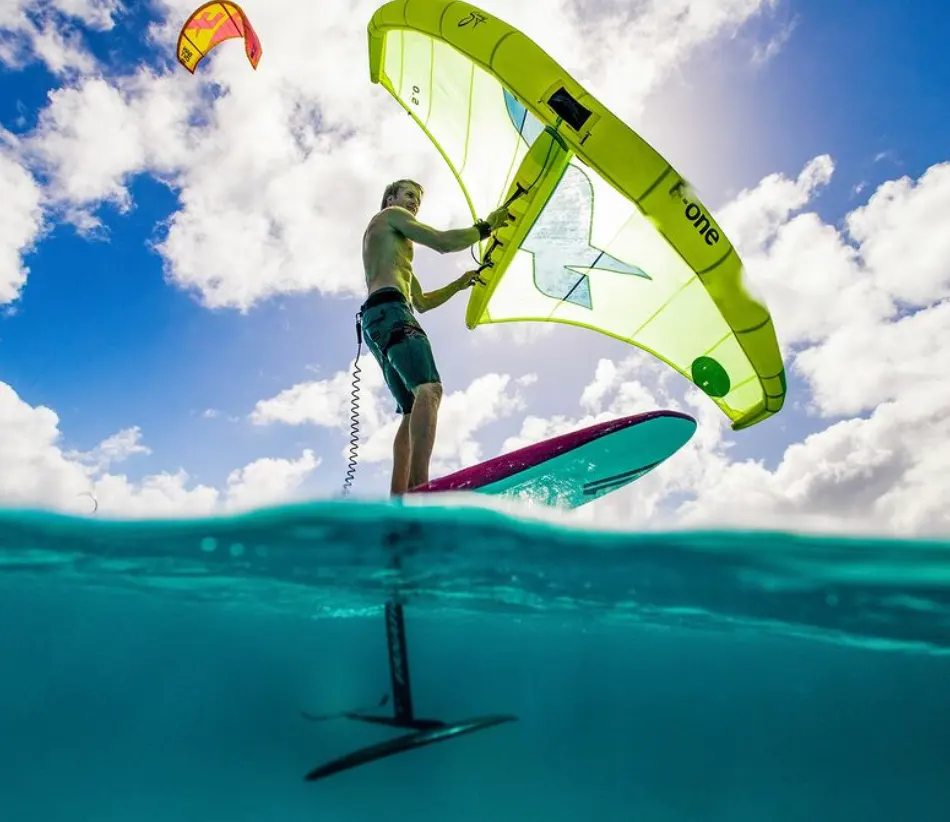 Wingfoilen op Bonaire Persoon die op Bonaire aan het wingfoilen is, wat de opwinding van de sport laat zien. Huur materiaal of neem lessen bij onze partner en geniet van speciale kortingen op pick-up verhuur bij Pickup Huren Bonaire.